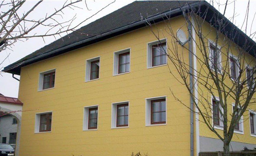 Ein Mehrfamilienhaus mit einer Zierer Putzstrukturfassade aus GFK in der Farbe Gelb.