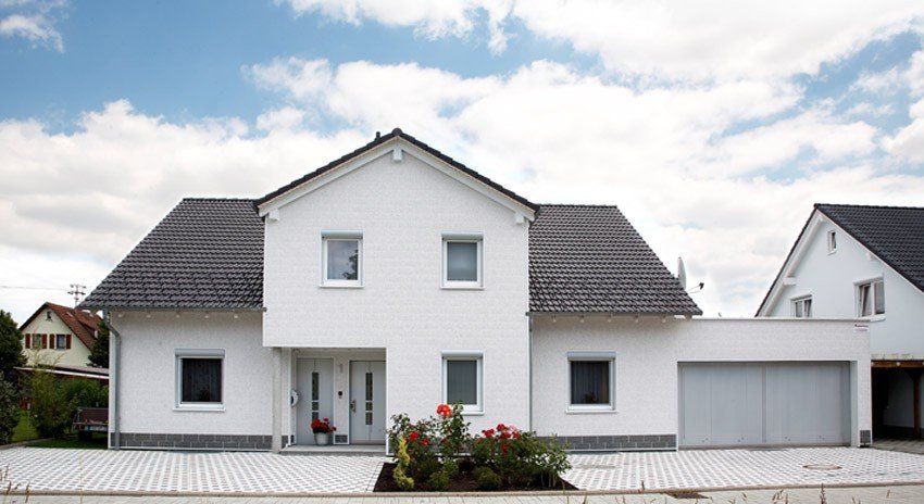 Ein Einfamilienhaus mit weißen Fassadenpaneele in Putzoptik. Der Sockel wurde mit der Farbe basalt abgesetzt.