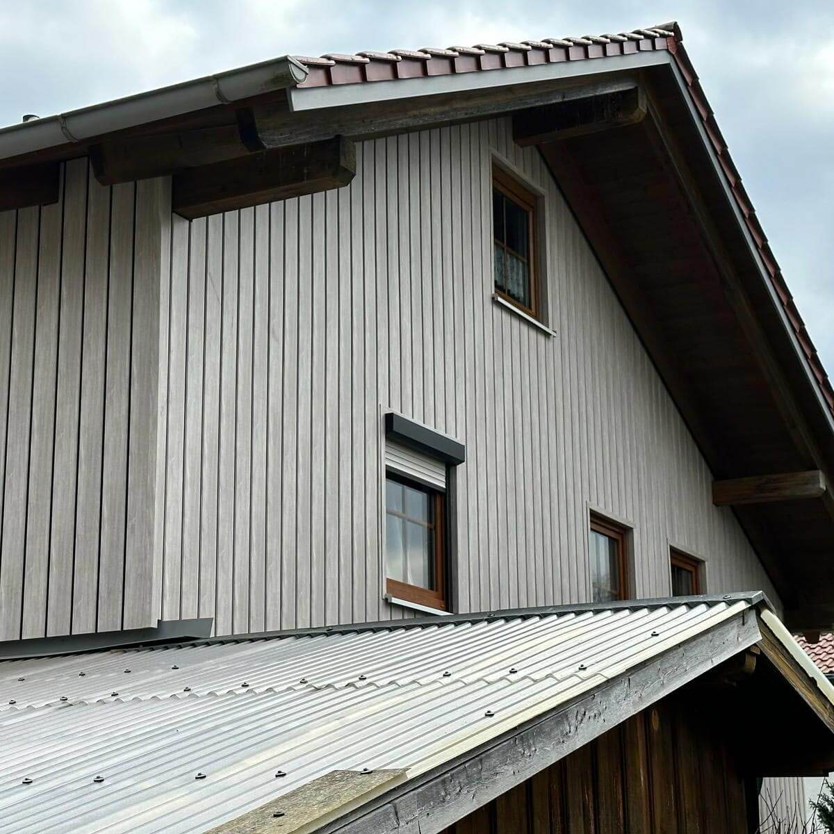 Klassisches Einfamilienhaus mit einer grauen Fassade in Holzoptik von vinyPlus Shadow. Der Fugenbereich bzw. Paneelrand ist zum Erreichen einer Rhombusschalung-Optik schwarz unterlegt.