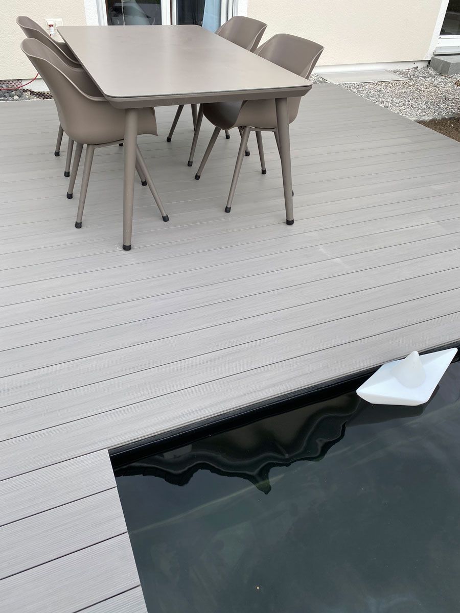 An einen Pool angebundene graue Terrasse mit einem Tisch und Stühlen.